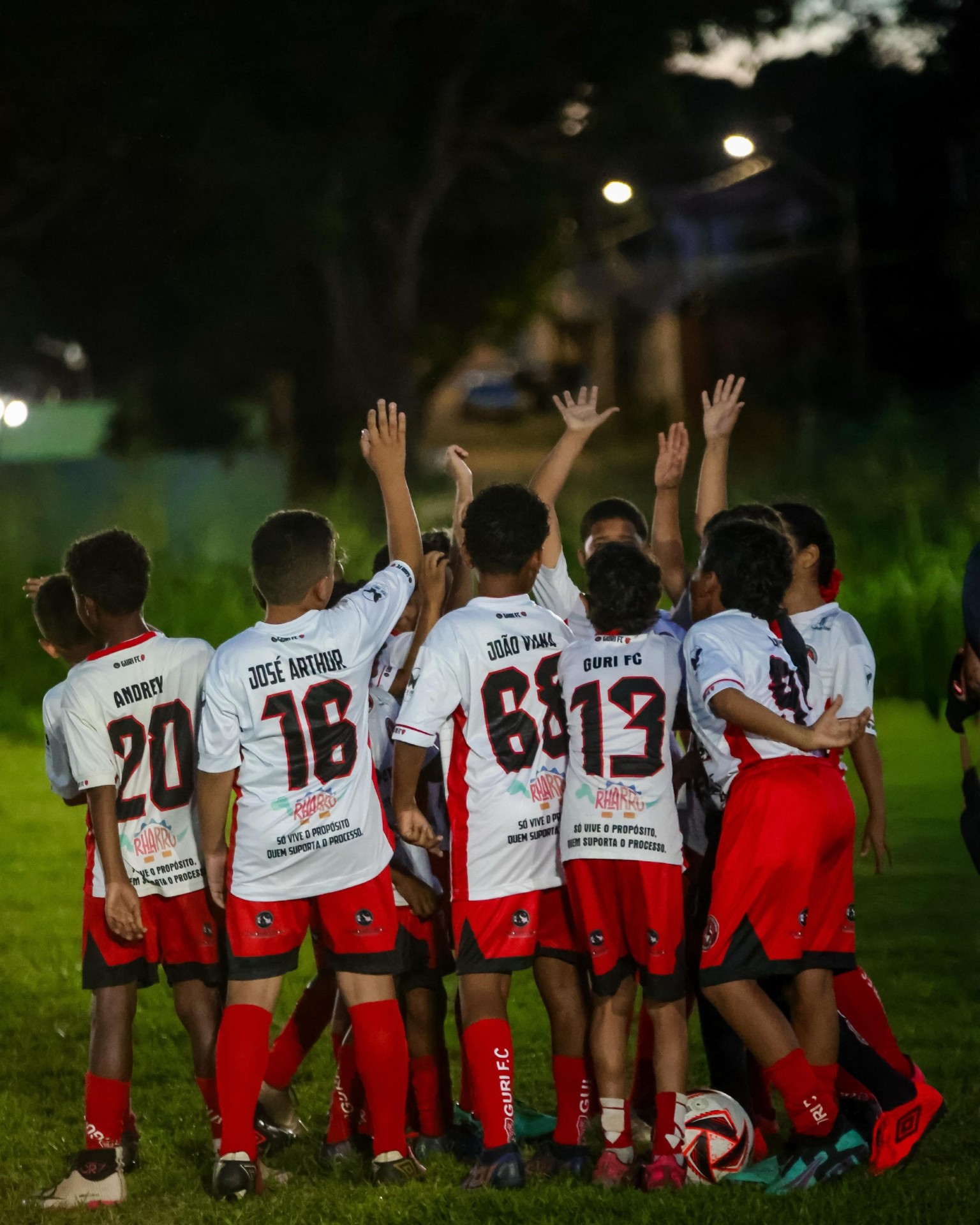 Equipe de futebol de base comemorando reunida em campo à noite